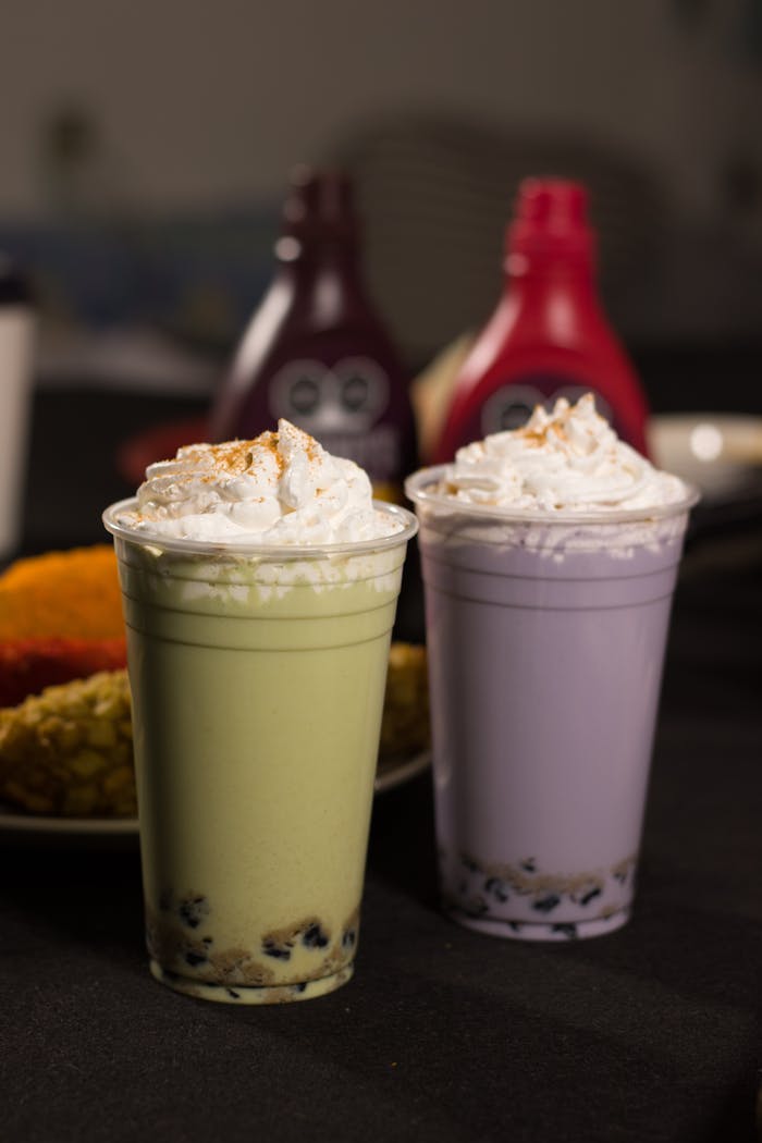 Two colorful boba milk teas with whipped cream, featuring vibrant green and purple colors.