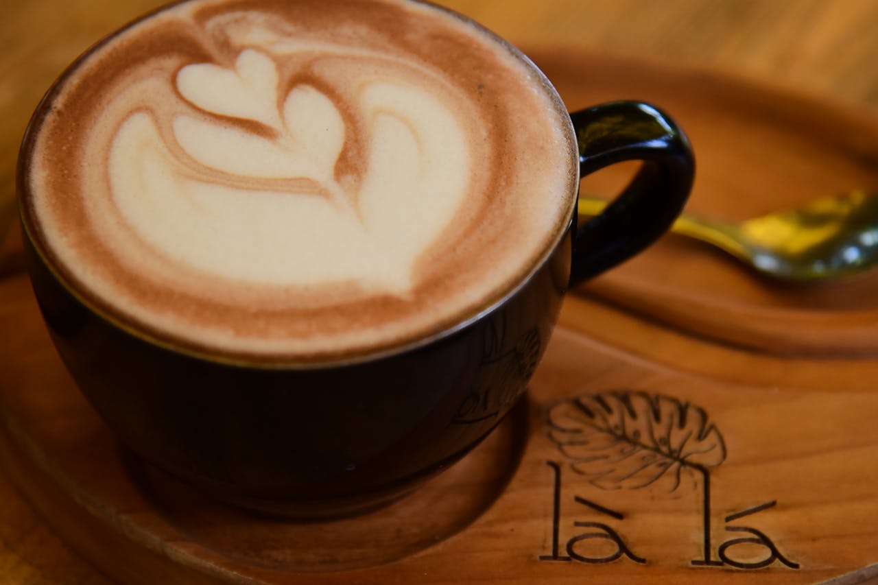 Close-up of a latte with intricate heart-shaped foam art in a black cup on wooden table.
