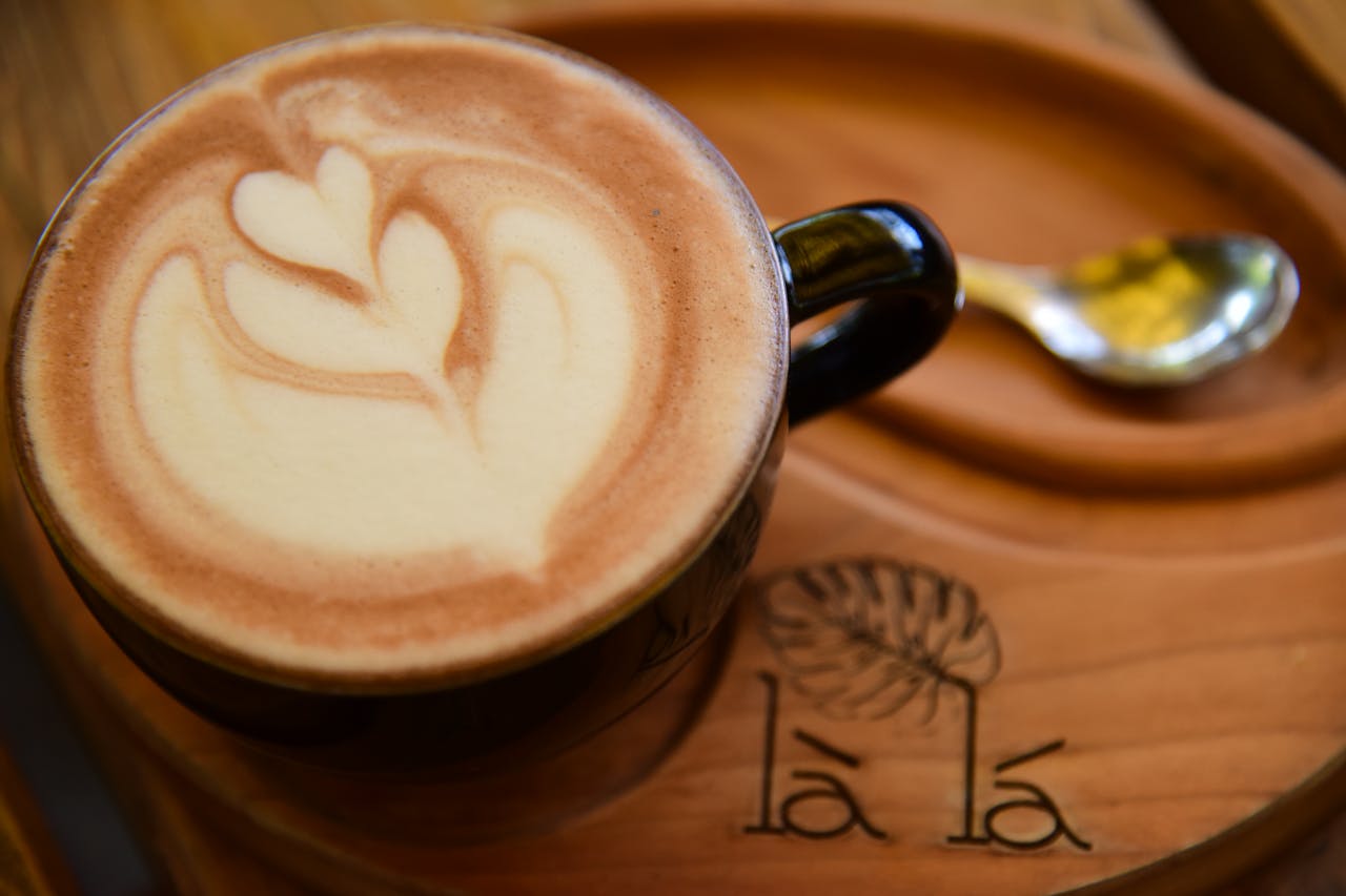 Close-up of a latte with intricate heart design art on a wooden tray in a cozy café setting.