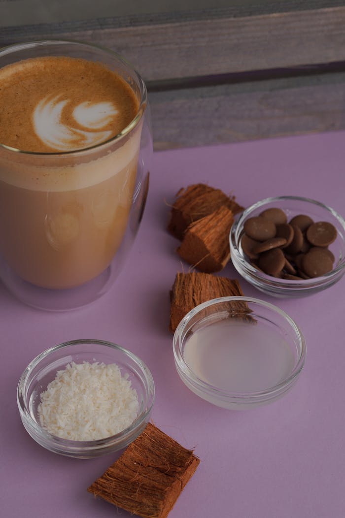 Close-up of a latte with coconut, chocolate, and other ingredients on a pastel surface.
